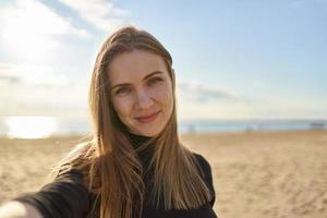 jolie femme aux cheveux longs regardant la caméra et souriant en soirée ensoleillée dans l'océan photo