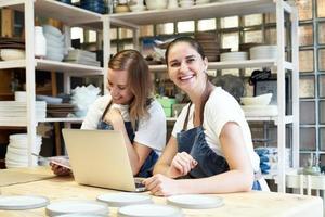 deux femmes entrepreneures souriantes avec ordinateur portable dans une salle de travail artisanale. portrait de femme souriante joyeuse photo