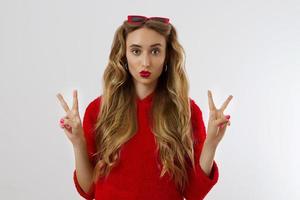 jeune femme en sweat à capuche rouge isolé sur fond blanc. concept de mode et de style. geste de signe de paix. heureuse belle fille à lunettes de soleil rouges. maquillage et beauté. modèle glamour. embrasser le visage photo