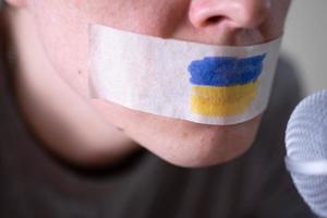 bande sur sa bouche avec le drapeau de l'ukraine, essayant de parler dans un microphone. photo