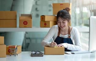 entrepreneur de petite entreprise asiatique PME écrivant l'adresse sur une boîte en carton sur le lieu de travail entrepreneur de petite entreprise PME, travaillant avec une boîte à la maison.