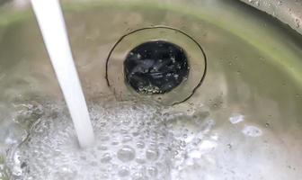 l'eau courante d'un robinet d'eau dans le drain d'un évier chromé. photo