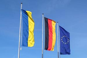 les drapeaux de l'ukraine, de l'allemagne et de l'union européenne volent côte à côte contre le ciel bleu. photo