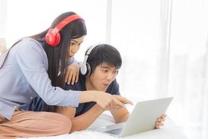 un jeune couple asiatique heureux est assis dans son lit et aime regarder des films sur un ordinateur portable sur fond blanc. photo