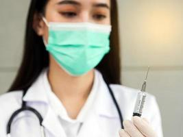 une femme médecin ou infirmière avec un masque chirurgical et un stéthoscope en flou tient une seringue, gros plan sur une seringue dans sa main. photo
