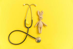 lapin jouet de conception simplement minimale et stéthoscope d'équipement médical isolé sur fond jaune. concept de médecin pour enfants de soins de santé. symbole du pédiatre. disposition de la vue de dessus à plat, espace de copie photo