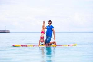 petite fille et jeune papa s'amusent sur une planche de surf photo