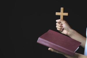 femme priant tout en tenant la bible et la croix, priez le matin, femme priant avec les mains ensemble sur le fond du lever du soleil. photo