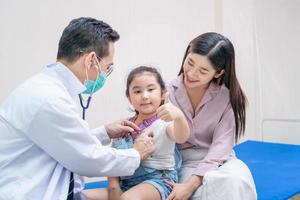 enfant fille patiente visite médecin avec sa mère, médecin pédiatre examinant un petit patient à l'aide d'un stéthoscope photo