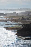 falaise rocheuse naturelle près du temple pura batu bolong avec vague frappant sur le littoral à bali photo