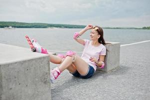 portrait d'une belle femme assise sur le sol à côté d'un cube en béton portant des rollers et des vêtements décontractés. photo