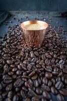 tasse en cuivre remplie de café expresso au centre de grains de café crus étalés sur une table rustique photo