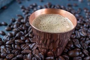 tasse en cuivre remplie de café expresso au centre de grains de café crus étalés sur une table rustique photo