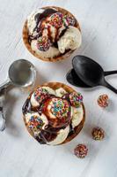 boules de crème glacée à la vanille avec des morceaux de bonbons colorés et du sirop de chocolat dans un bol à cône gaufré sur fond blanc rustique photo