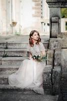 mariée.jeune mannequin avec une peau et un maquillage parfaits, fond blanc. belle mariée sur fond escalier blanc. une femme vêtue d'une longue robe blanche est assise dans les escaliers. photo