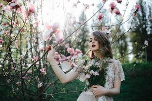 très belle fille la mariée sous un voile, robe de mariée beige près de l'arbre sakura regarde vers le bas, nature photo