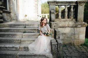 mariée.jeune mannequin avec une peau et un maquillage parfaits, fond blanc. belle mariée sur fond escalier blanc. une femme vêtue d'une longue robe blanche est assise dans les escaliers. photo