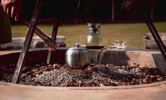 homme faisant du café goutte à goutte avec une bouilloire sur un poêle à charbon au camping. photo