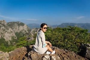 une femme asiatique avec des lunettes de soleil est assise au sommet de la montagne. photo