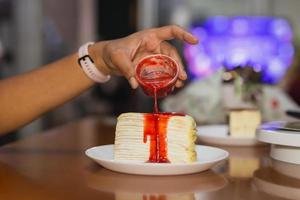 main féminine versant de la sauce aux fraises sur le gâteau de crêpe. photo