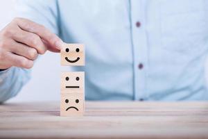 homme d'affaires choisit un sourire émoticône icônes visage heureux symbole sur bloc de bois , services et concept d'enquête de satisfaction client photo