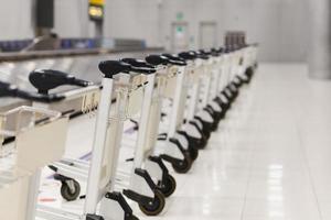 chariots à bagages vides de l'aéroport se garant derrière la ligne d'avertissement dans la zone de retrait des bagages du terminal. photo