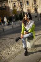 jeune femme écoutant de la musique avec un smartphone dans la rue et tenant un café à emporter photo