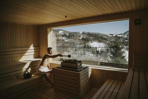 jeune homme versant de l'eau sur des pierres chaudes dans le sauna photo