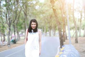 belle femme asiatique en robe blanche marchant et souriant dans le parc naturel. une fille thaïlandaise ou une fille chinoise profite de vacances dans le jardin photo