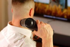 homme avec un pistolet de massage assis sur un canapé faisant un massage, mise en scène de style de vie photo