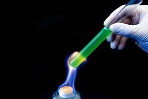 un tube à essai de laboratoire avec une solution verte dans la main d'un homme est chauffé au feu