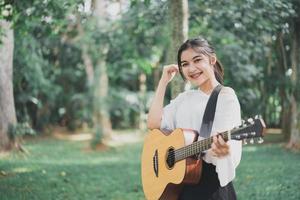 jeune femme asiatique jouant de la guitare et chanter de la musique dans le parc, femme asiatique jouant de la guitare au jardin photo