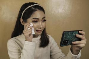 triste adolescente qui pleure en vérifiant son téléphone assis. femme asiatique regardant l'écran du smartphone versant des larmes photo