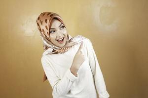 joyeuse jeune femme asiatique musulmane pointant au-dessus pour copier l'espace avec le sourire photo