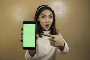 belle fille asiatique est choquée de montrer un écran vert dans un smartphone avec une chemise blanche photo