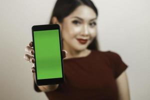 jeune femme asiatique heureuse et souriante montrant et pointant vers un écran blanc vert. photo