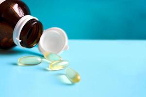capsules de médecine de gel de couleur ambre ou pilules nutritives de supplément jaune avec bouteille de pilule renversée sur fond bleu, concept pharmaceutique médical et de soins de santé. photo