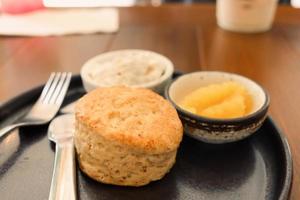 délicieux scone avec de la confiture et de la crème caillée dans une assiette noire sur une table en bois. photo