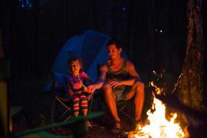 papa et sa fille s'assoient la nuit au coin du feu en plein air en été dans la nature. voyage de camping en famille, rassemblements autour du feu de camp. fête des pères, barbecue. lanterne et tente de camping photo