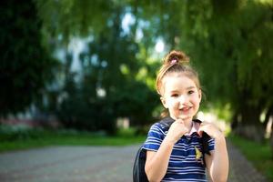 une petite fille d'apparence caucasienne en uniforme scolaire avec un sac à dos regarde dans le cadre. concept de retour à l'école. primaire, développer des activités pour les enfants d'âge préscolaire. espace pour le texte photo