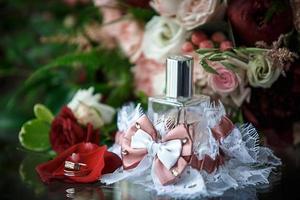 accessoires de mariage pour la mariée et le marié un bouquet de roses rouges, roses et blanches, une boutonnière, des alliances en or, une jarretière en dentelle avec un arc, du parfum. bijoux, fleuristerie. espace pour le texte photo