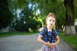 une petite fille d'apparence caucasienne en uniforme scolaire avec un sac à dos regarde dans le cadre. concept de retour à l'école. primaire, développer des activités pour les enfants d'âge préscolaire. espace pour le texte photo