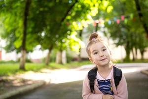 une petite fille d'apparence caucasienne en uniforme scolaire avec un sac à dos regarde dans le cadre. concept de retour à l'école. primaire, développer des activités pour les enfants d'âge préscolaire. espace pour le texte photo