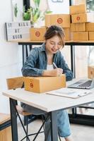 une femme entrepreneure asiatique emballe le produit dans la boîte sur son lieu de travail à domicile. le propriétaire d'une entreprise adolescente travaille à la maison, beaucoup de choses à faire aujourd'hui à la maison. démarrer le concept de PME. photo