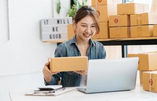 une femme entrepreneure asiatique emballe le produit dans la boîte sur son lieu de travail à domicile. le propriétaire d'une entreprise adolescente travaille à la maison, beaucoup de choses à faire aujourd'hui à la maison. démarrer le concept de PME. photo