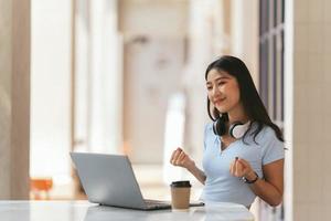 jeune femme avec ordinateur portable exprimant son enthousiasme dans le bureau à domicile, une femme asiatique excitée se sent euphorique en lisant de bonnes nouvelles en ligne. photo