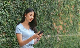 femme asiatique heureuse souriante et tenant un téléphone portable tout en étant assise dans un café d'été de rue. photo