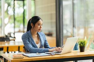 portrait d'une jeune femme asiatique travaillant sur un ordinateur portable et un rapport financier au bureau. photo