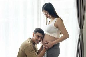 jeune femme enceinte avec son mari embrassant et attendant un bébé à la maison photo