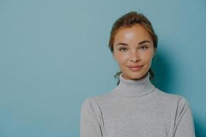 portrait d'une femme souriante avec du maquillage et une peau saine et éclatante vêtue d'un col roulé gris photo